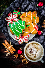 Traditional christmas sweet treats, colorful sugar glazed homemade gingerbread cookies with xmas tree, decoration, spices and coffee latte mud on classic wooden background copy space top view