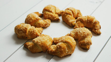 From above view of fresh crunchy croissants placed in circle of white wooden background 