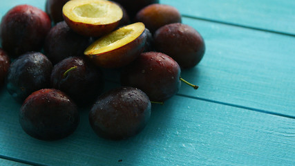 From above shot of pile of delicious and juicy plums composed with few cut halves on blue-colored wooden table