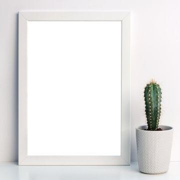 Photo of a white mockup frame against the background of an empty wall with a cactus with a gray flowerpot with a sweater pattern
