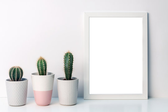 Photo of a white mockup frame on a background of empty copy space wall with cactuses of a gray pot with a pattern of sweater and one pink terrazzo