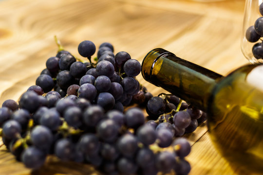 Image of a glass, freshly picked failed processing, black grapes on a wooden background and an empty bottle