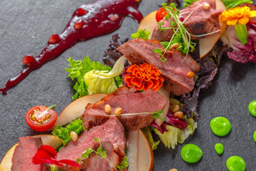 Tasty sliced roast duck breast with fresh vegetable salad closeup on a plate.