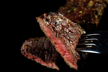 Close up of medium rare beef steak piece on a fork . Spiced with peppercorns and herbs. More fried...