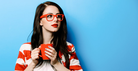 portrait of the beautiful young woman with red cup of coffee on the blue background