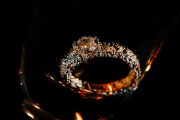 Wedding ring in champagne glass with golden bubbles. Close-up view on black background