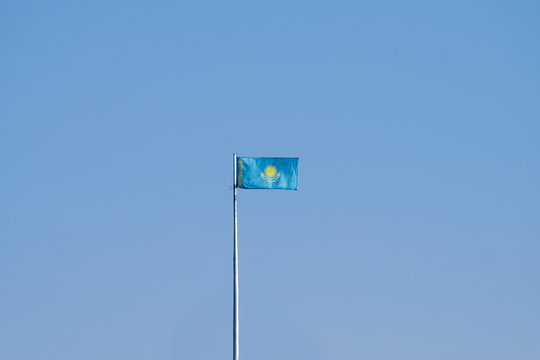Flag of Kazakhstan on flagpole against the blue sky.