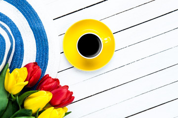 Cup of coffee with hat and tulips on white wooden table.