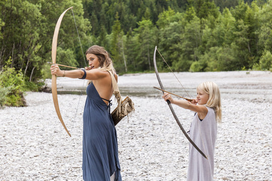 Mother and daughter aiming with bow and arrow in forest