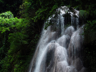 Obraz premium A close up view of cascading water falling over the rocks and sunlight of a natural waterfall. Shot in Thailand
