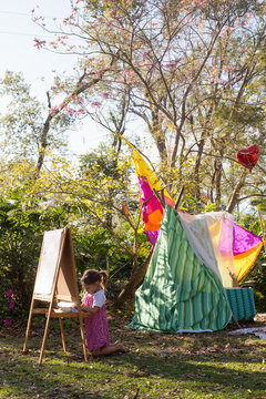 A pre-school girl painting at an easel in a garden. 