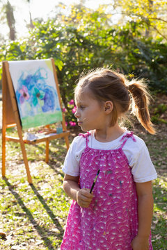 A pre-school girl painting at an easel in a garden. 