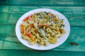 Pasta with vegetables and cheese in a white plate on a green background