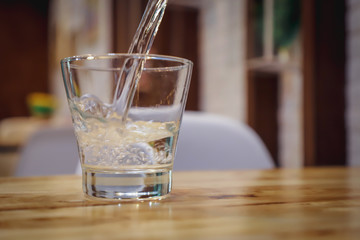A glass of pure fresh water is poured into a glass, the background dinning room