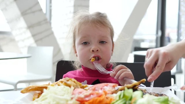Cute little child girl eating french fries potato in fast food cort