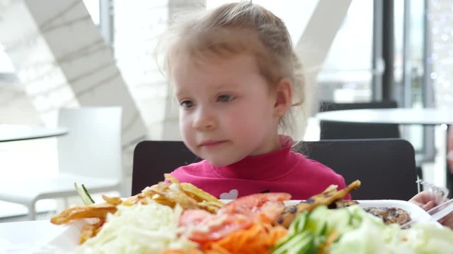 Cute little child girl eating vegetables instead of meat in fast food cort