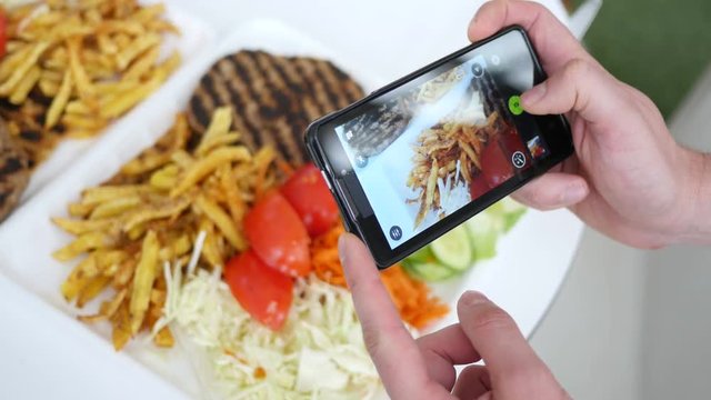 Man take a photo picture of food via his smartphone above a dish