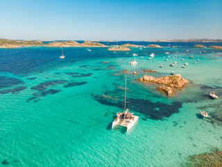 Drone aerial view of catamaran sailing boat in Maddalena Archipelago, Sardinia, Italy. Maddalena Archipelago is composed of Razzoli, Santa Maria and Budelli islands. - obrazy, fototapety, plakaty