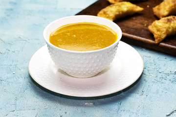 a bowl of spiced algerian vegetable soup named (Harira) and meat bourak named bourek laajine on wooden cutting board
