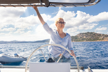Attractive blond female skipper navigating the fancy catamaran sailboat on sunny summer day on calm blue sea water. Luxury summer adventure, active nautical vacation.