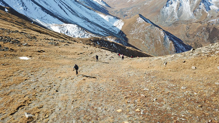 Tourists climb the mountainside. Climbing the peak. Visible land, dry grass and snow. Walk on mountains.