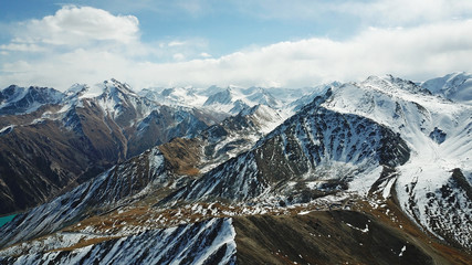 Stone and snow-capped mountains. Blue sky and clouds. Shooting with the drone. Panorama of snowy peaks and rocky mountains. Sharp stones and a gorge are visible.