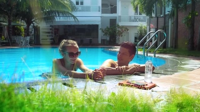 guy drinks water girl laughs and swims across pool