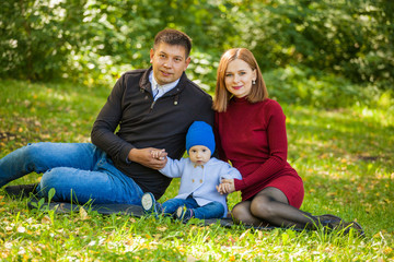 Naklejka na ściany i meble mom, dad and baby are sitting on the grass in the park. Family weekend in the fall