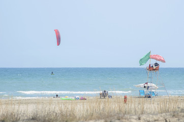 Sunny day, with blue sky, of summer at the beach of Castellon (Spain). Kiteboarder propelled by the air flows of Mediterranean sea. Lookout of beach guard. People in vacations sunbathing.