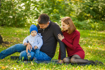 Naklejka na ściany i meble mom, dad and baby are sitting on the grass in the park. Family weekend in the fall
