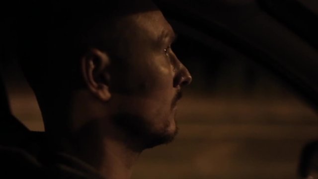 A close side view of a mature man driving a car at night