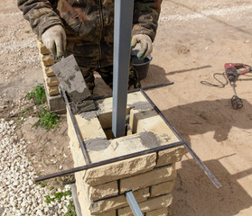 The worker is laying bricks on the fence