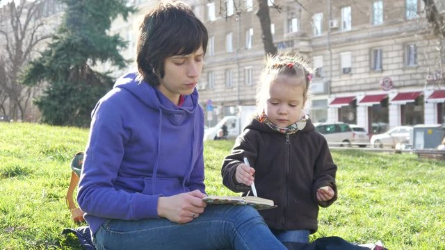 Mom spending time with a child sit on grass in a park drow in notebook