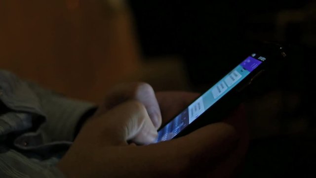 Man typing message via smartphone display touchscreen at night
