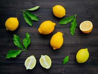 Fresh lemons and  lemons leaves on dark wooden background.