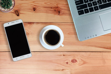 Black coffee in white cup and laptop computer and cactus and Mobile Phone or Smartphone with blank screen on wooden floor, Top view, copy space