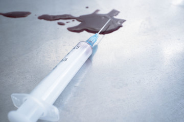 syringe with blood and a puddle of blood on the medical table