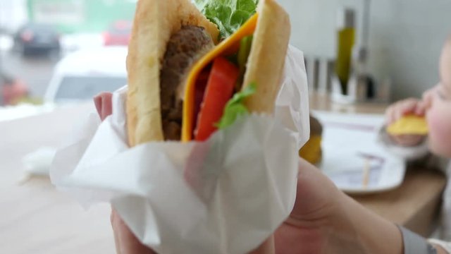 Open paper packaging and eat fresh juicy sandwich at a fast food restaurant