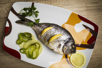 Dorada fish cooked in the oven with lemon, pimento and green onion served on a tray on a wooden table ready to eat
