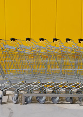 Stack of new shiny shopping carts in a supermarket with yellow wall in background