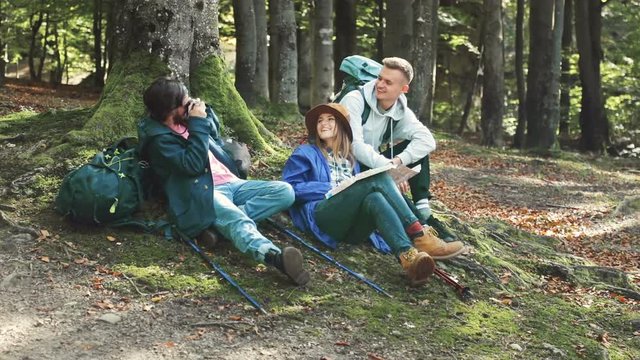 Group of cheerful travellers taking pictures while resting near tree, spending great time together on fall vacation in mountanious region