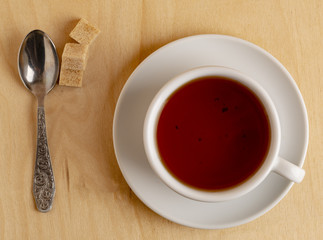Cup of hot tea on a saucer, fresh biscuits, brown sugar and a cloth napkin.
