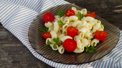 Delicious pasta with tomatoes and greens on wooden background.