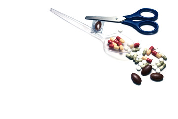 a plastic spoon with medicines tablets and blue scissor with pile of  pills on white background isolated