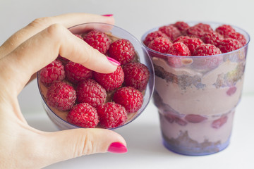 a hand with a beautiful manicure holds a cake in a Cup with berries and chocolate