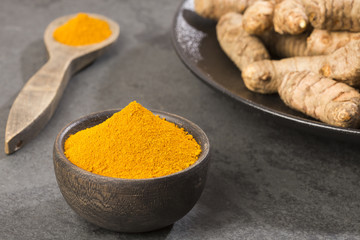 Turmeric powder and fresh turmeric on wooden background