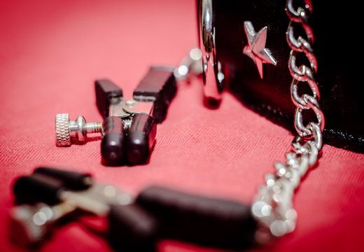 bdsm accessory human collar and accessory nipple clasp with metal chain on a red background close-up