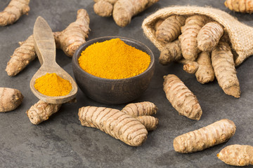 Turmeric powder and fresh turmeric on wooden background