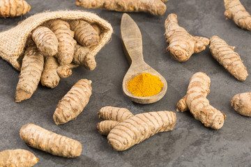 Turmeric powder and fresh turmeric on wooden background