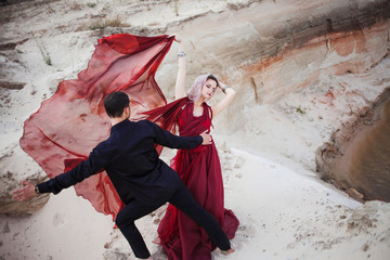 Love and passion, concept. Beautiful young couple dancing in desert. The man in black and woman in...
